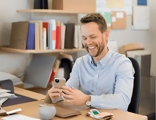 The Vital Role of Technology in Betting Security for Slot Sites like VSlots88 A Caucasian man with a broad smile leans back in his chair fingers resting lightly on his smartphone surrounded by a neatly organized desk - The Vital Role of Technology in Betting Security for Slot Sites like VSlots88