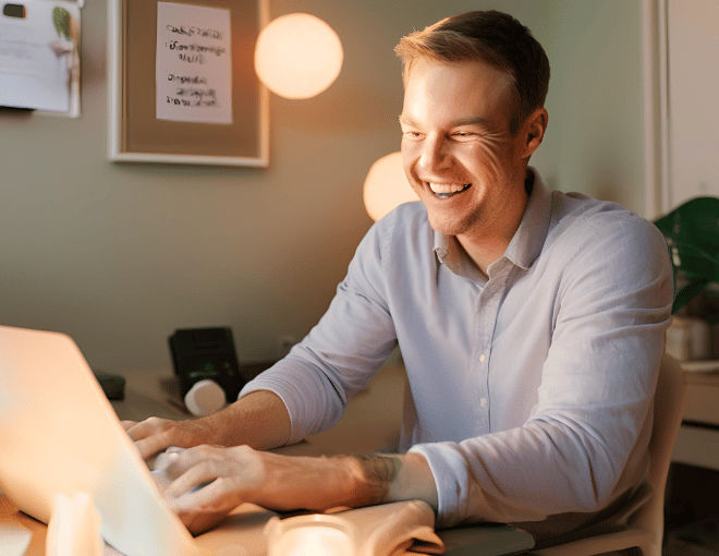 A cheerful Caucasian man seated in a cozy home office beams at his laptop screen his face illuminated by its soft glow - Leveraging AI and Machine Learning for Safer Betting and Lottery Experiences